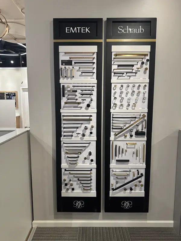Emtek and Schaub cabinet hardware display panels mounted side by side on a showroom wall